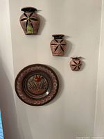 Three small half pot wall hangings and one decorative Mexican pottery plate mounted on white wall, shown together