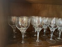 Group view of multiple clear crystal stem glasses in a wooden cabinet with faceted stems showing shape variety.
