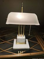 Front view of the entire vintage brass and Carrera marble banker's lamp with frosted white glass shade lit