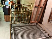 Headboard and metal slatted frame rails placed on floor, showing the vertical bars and brass finish