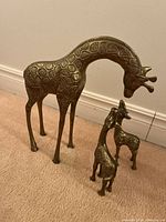 Three brass giraffe figurines displayed on carpeted floor against white wall.
