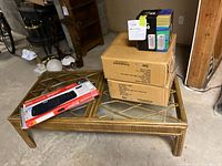 Photo showing the rattan coffee table with glass top, two unopened boxes of brown velvet hangers, new Microsoft keyboard on top, and two boxes presumably containing speakers.