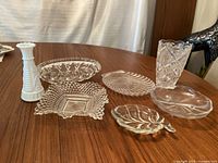 Photo of two vases and five clear glass serving plates with various etched and cut designs on wooden table.