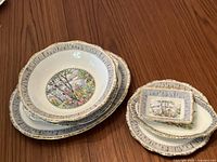 Top-down photo showing stack of four round and oval plates and bowls with gold trim, birch tree design.