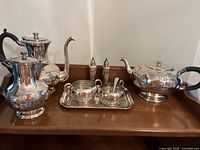 Full tea and coffee service set displayed on a wooden surface showing all items in the lot including salt and pepper shakers, pots, creamer and sugar bowl on tray.