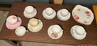 Nine assorted vintage teacups and eight matching saucers arranged on table, various floral designs.