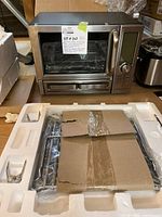 Wolfgang Puck convection oven on countertop with original styrofoam packaging containing oven racks and accessories in cardboard wrap visible.