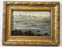 Front view of the antique oil painting on board depicting mountain landscape with water and rocky foreground in a gold-tone carved wooden frame.