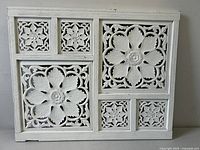 Front view of the rectangular white carved wooden panel with intricate floral designs in multiple sections.