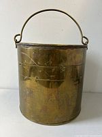 Front view of the antique solid brass bucket showing curved handle and studded body.