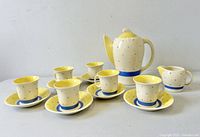 Full set arranged including coffee pot, creamer, five cups and saucers on white surface with visible pattern and colors.