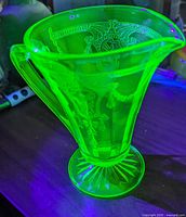 Art Deco Anchor Hocking Vaseline glass cream jug glowing under UV light, showing intricate molded patterns and sunburst pedestal base.