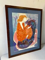 Framed colorful lithograph featuring an abstract female figure, shot from an angle showing the entire artwork and frame.