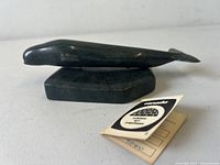 Side angle of black whale carving on stone base with original card and sticker next to it