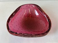 Top view of the raspberry red Murano glass triangular bowl showing the smooth curved edges and embedded control bubbles.