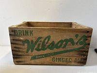 Front side of wooden crate with green text 'Drink Wilson's Since 1875 Ginger Ale'.