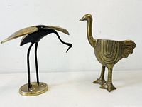 Front view of brass ostrich and brass/black metal crane figurines on white background.