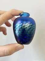 Front and side views of the small iridescent blue-purple glass bud vase showing the scaled pattern and rounded neck opening.