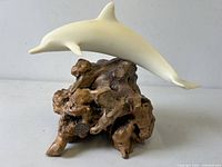 Front-right angled view of white dolphin sculpture on natural burlwood base.