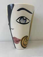 Front angle showcasing the abstract stylized lady's face with blue eye, pink lips, and yellow-black hair swirl design on the cream porcelain surface.