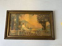 Frontal view of framed art print depicting a woman seated on a stone balustrade with a sunset mountainous landscape in the background. The frame is visible with decorative scrolling and some slight wear.