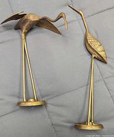 Photo of both brass crane bird statues lying on a soft surface to show front and side views.
