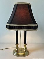 Front view of the vintage table lamp showing dual black columns, brass base, and black fabric shade with decorative trim.