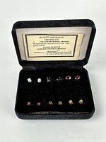 Open case showing six pairs of gemstone earrings and quality card