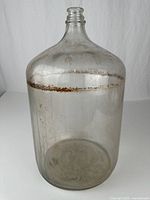 Front view of clear glass carboy showing overall shape and mineral deposits