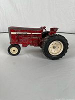 Left side view of red Ertl International Harvester tractor showing paint wear and missing steering wheel