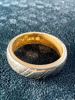 Ring resting on dark fabric showing exterior diagonal grooves and white gold finish, interior yellow gold visible