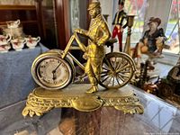 Full front view showing gilt-brass bicycle clock with gentleman figure on ornate brass base.