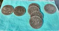 Photo of seven Canadian silver dollar coins on blue cloth. Coins include one Manitoba 1970 coin, four 1975 coins, one 1976 coin and one 1979 coin.