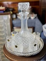 Full view of the decanter placed in the center of the round plated server surrounded by six small shot glasses, highlighting the diamond cut crystal pattern.