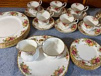 Overall view of six dinner plates stacked, side plates, six teacups on saucers, sugar bowl, creamer, and serving platter.