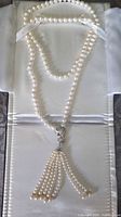 Full view of pearl necklace laid out showing strand, connector and tassel pendant