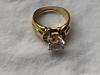 Close-up front angle of 18K gold plated vintage ring with clear round-cut stone mounted in a square setting, visible wear on band.