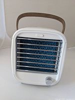 Front view of the white portable air conditioner showing silver bars over blue water curtain and fan speed dial below.