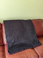 Purple alpaca blanket folded and placed on a red leather couch, showing texture and color in diffused light.