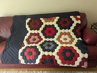 Full front view draped over sofa showing hexagon flower patchwork and navy quilted backing folded over