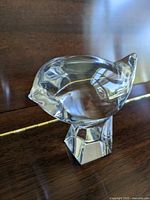 Clear crystal bird figurine on a wooden surface, showing the side profile with a square base.
