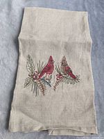 Full view of natural-colored embroidered tea towel showing two cardinals perched on branches with berries embroidered towards one end.