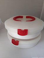 Two stacked white plastic carriers with red locking handles and clasps, photographed against a white background