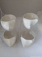 Four ceramic planters shaped like hedgehogs arranged in a square formation on clear blocks, showing front view of the planters' faces with closed eyes and smooth surfaces.