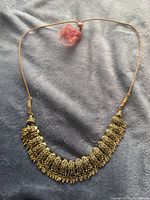 Full view of the gold coloured Indian necklace laid flat on grey fabric background showing the entire design and pink tassel at closure.