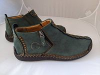 Pair of men's green leather boots with brown stitch detailing, side zipper, and printed emblem on outer side.