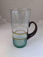 Full view of the tall clear glass pitcher showing gold bands and tinted amber handle.