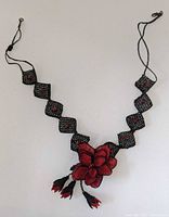 Front view of the handmade necklace showing black diamond-shaped bead segments with red centers and the central red and black beaded flower pendant with tassels.