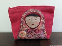 Front view of red embroidered pouch showing detailed stylized female face design.