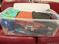 Closed clear plastic bin filled with assorted fabric pieces on a red couch.